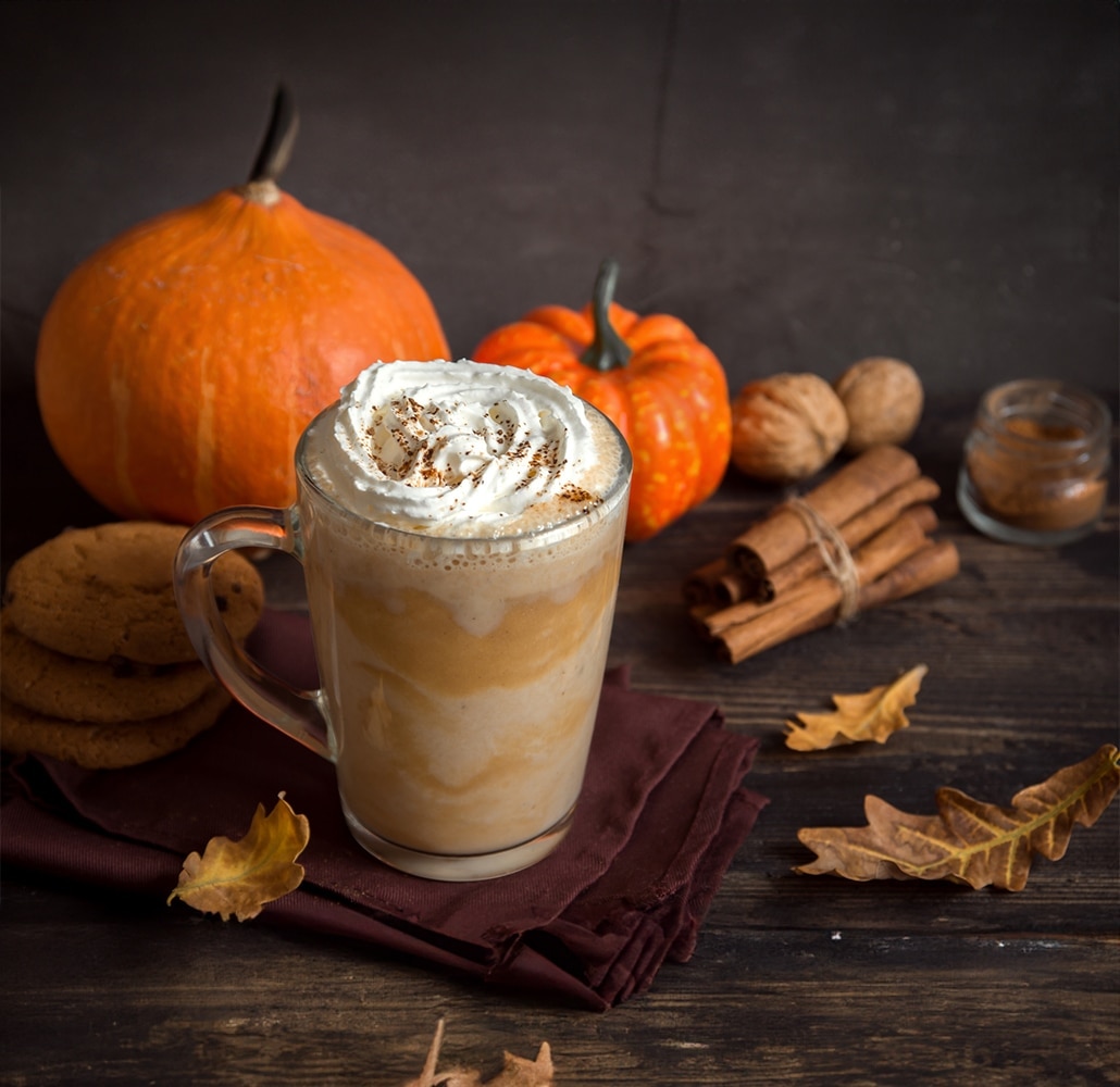 Taza de café Pumpkin Spice con nata montada rodeada de calabazas de otoño
