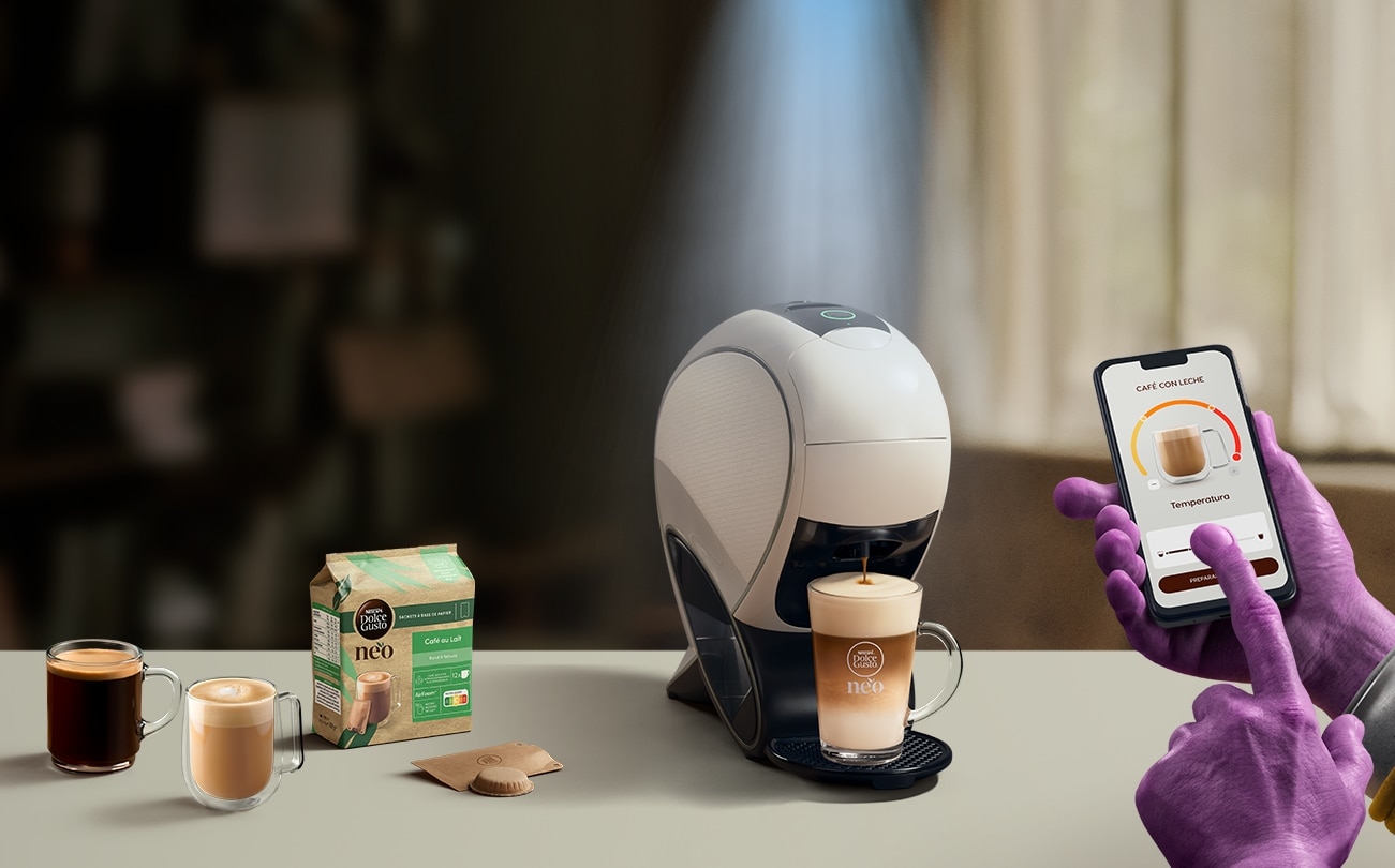 Una mano alienígena utilizando la aplicación NESCAFÉ Dolce Gusto para personalizar una bebida. Cafetera inteligente NEO Latte, pack de café y bebidas.