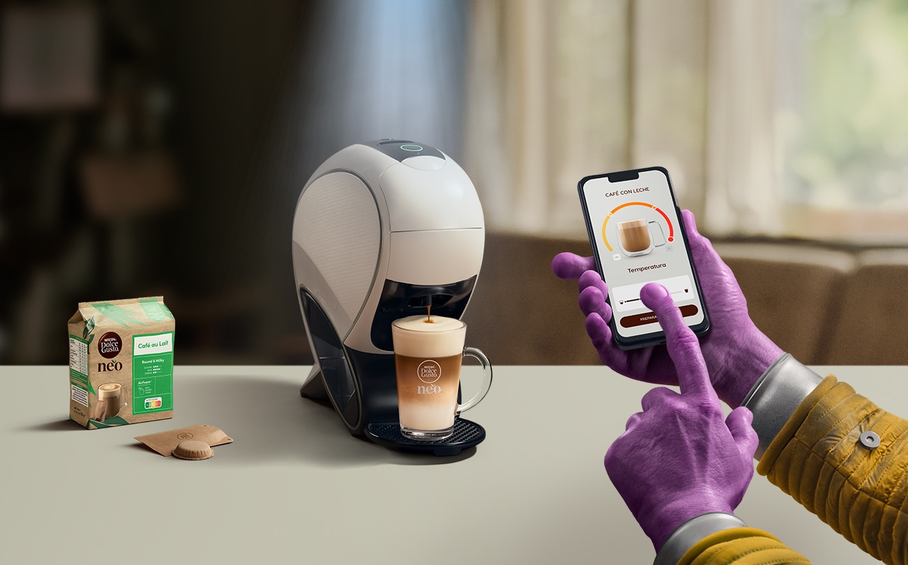 Una mano alienígena utilizando la aplicación NESCAFÉ Dolce Gusto para personalizar una bebida. Cafetera inteligente NEO Latte, pack de café y bebidas.