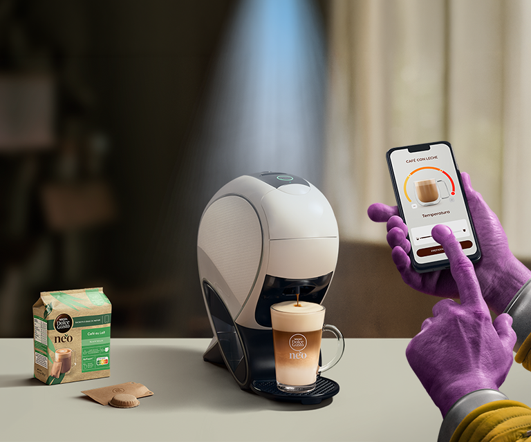 Una mano alienígena utilizando la aplicación NESCAFÉ Dolce Gusto para personalizar una bebida. Cafetera inteligente NEO Latte, pack de café y bebidas.