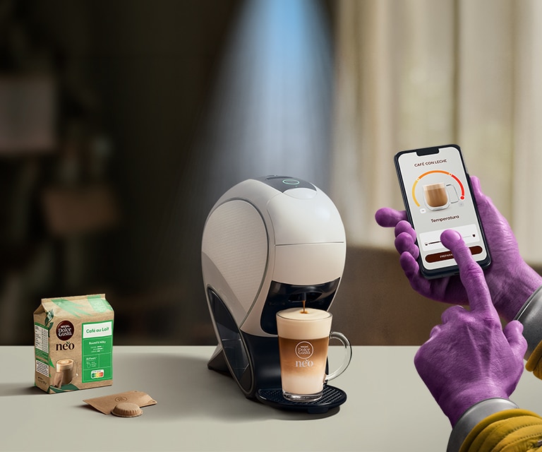 Una mano alienígena utilizando la aplicación NESCAFÉ Dolce Gusto para personalizar una bebida. Cafetera inteligente NEO Latte, pack de café y bebidas.